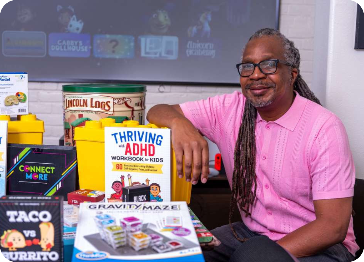 Person in pink shirt seated beside a display of educational and ADHD-related children's books and games on a table.